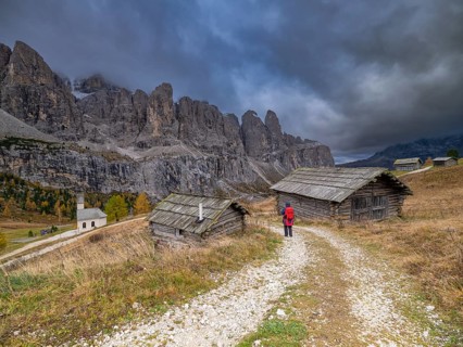 Hiker in front of two huts at the Gardena Pass, chapel, gloomy clouds, Passo Gardena, autumn, Sella