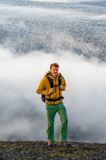 Young man in front of impressive landscape at sunset, fog, clouds moving around, glacier ice of the