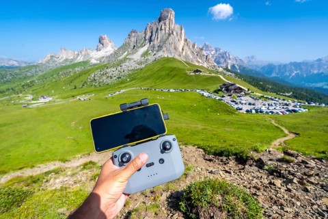 Hand piloting a drone with a smartphone attached to the controller in the scenic landscape of giau