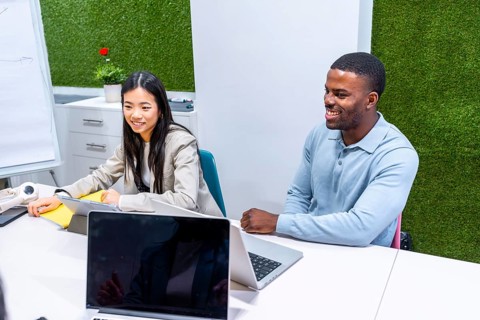 Two businesspeople are working together on a project in a modern coworking office, using laptops
