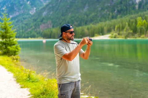 Tourist taking photos of the landscape at lake dobbiaco during summer holidays in the italian