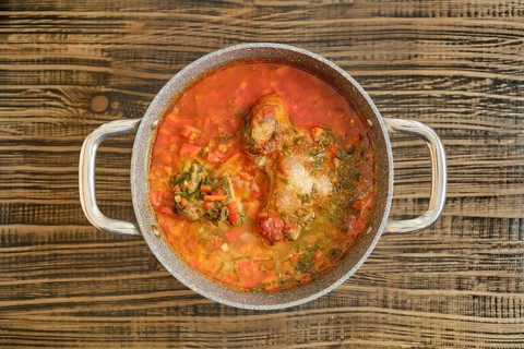 A hearty turkey stew with vibrant vegetables is simmering in a pot on a wooden surface. The rich