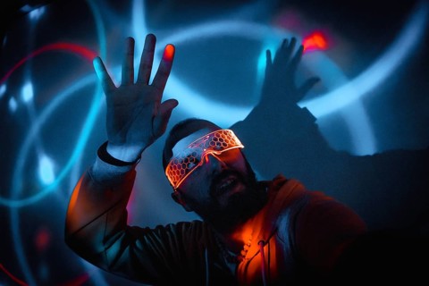 Cyberpunk man wearing illuminated goggles interacting with virtual reality game using augmented