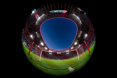 Overview, interior, floodlit match, behind-the-goal perspective, goal net, blue hour, fisheye shot,