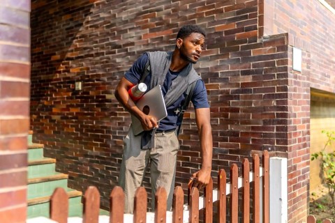 Young african businessman leaving a house in a residential district to go to work holding a laptop