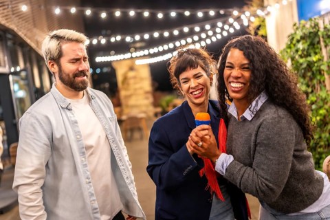 Multi-ethnic diverse friends enjoying singing karaoke outdoors in a bar terrace