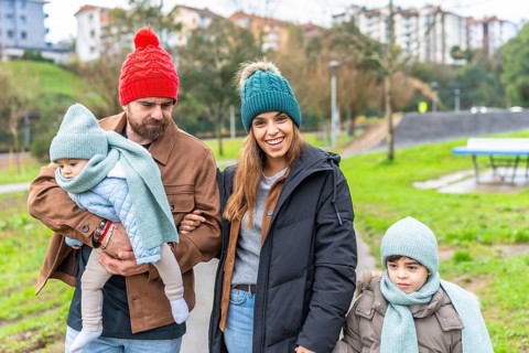 Smiling family enjoying a delightful winter walk in the park, bundled up in warm hats and scarves,