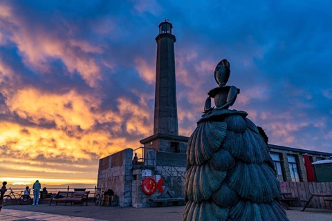 Bronze sculpture Mrs Booth The Shell Lady and the Margate lighthouse at sunset, Kent, England,