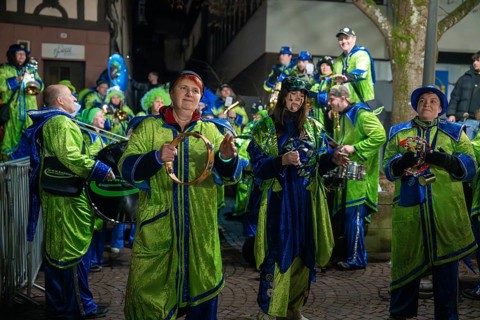 Music group in green and blue costumes with instruments at a night-time performance, carnival,