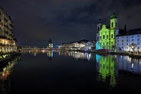Water tower and Jesuit church on the right with light installation, on the Reuss at dusk, Old Town,