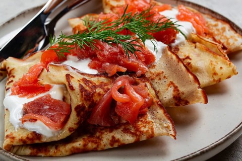Delicious pancakes with salmon and sour cream, breakfast, on a plate, rustic style, with cutlery