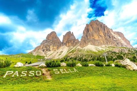 Green meadow with passo sella sign and the sassolungo group in the background, dolomites, italy