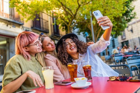 Three female beauty travelers taking selfie enjoying beverages on an outside cafeteria