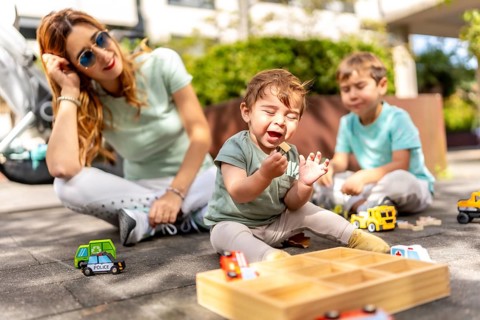 Young caucasian mother with baby and son playing sitting in a park