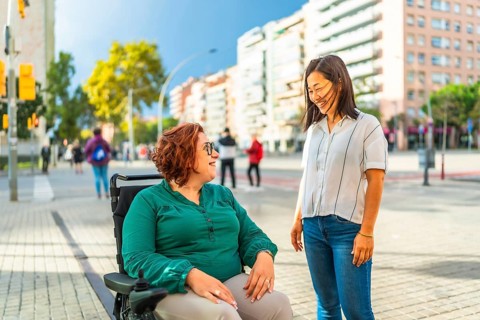 Woman with disabilities and asian caregiver talking relaxed in the city