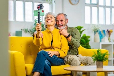 Happy senior couple during online meeting with the family using smartphone sitting on the sofa