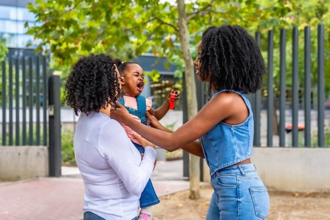 African schoolgirl crying in the park next to her mother and granny that is carrying her