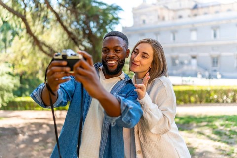 Cute multi-ethnic couple taking selfie with digital camera in a city view point