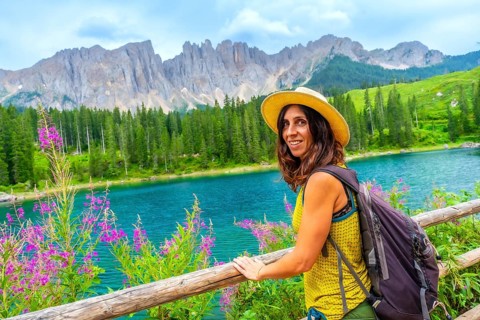 Female tourist with backpack and straw hat enjoying the landscape of lake carezza and latemar