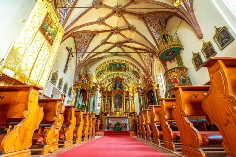 Interior of the church of st. Magdalena in val di funes, showing frescoes, pews and red carpet, in