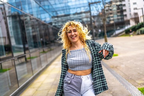 Carefree young woman with curly blonde hair enjoying dancing to urban music in a city street,