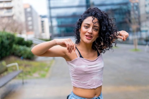 Curly haired woman dancing outside, performing a modern dance routine in an urban environment