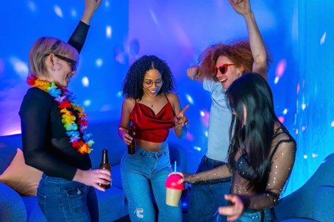 Cheerful multi ethnic friends dancing together and enjoying drinks at a home disco party with blue