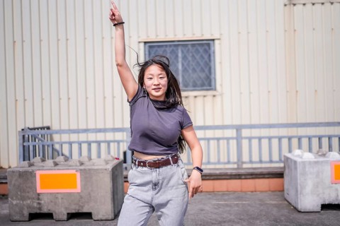 Asian young woman pointing to the sky dancing k-pop urban dance outside an industrial building in
