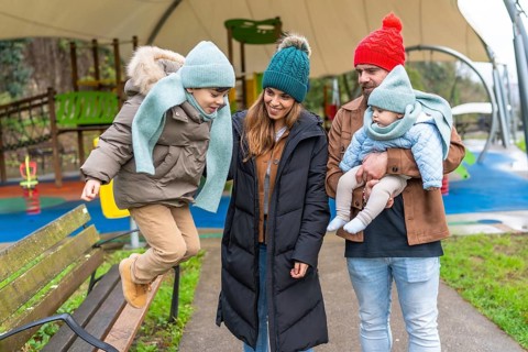 Smiling family enjoying a joyful winter day at the playground, with children happily jumping on a