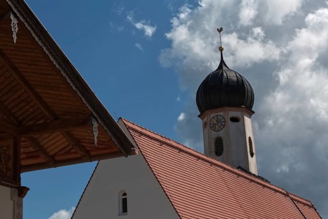 A baroque church tower and part of a roof in front of a blue sky with clouds, Wallgau, Bavaria,