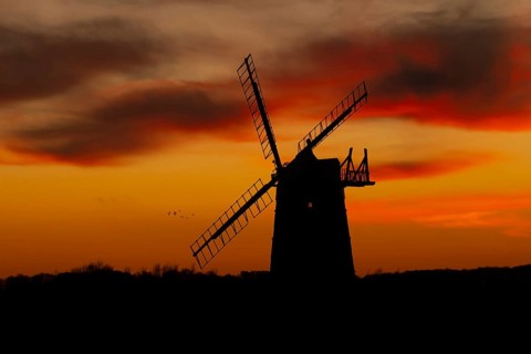Windmill silhouette at sunset with a red sky and clouds and a flock of Lapwing flying behind,