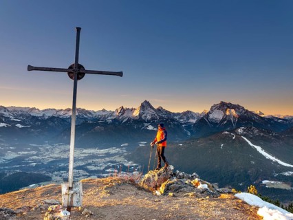 Mountaineers at the summit cross Rauher Kopf at sunrise, in the background the Berchtesgaden Alps,