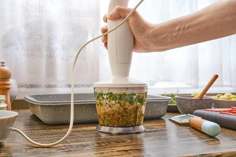 A hand blending device is being used to process fresh herbs and vegetables in a well-organized