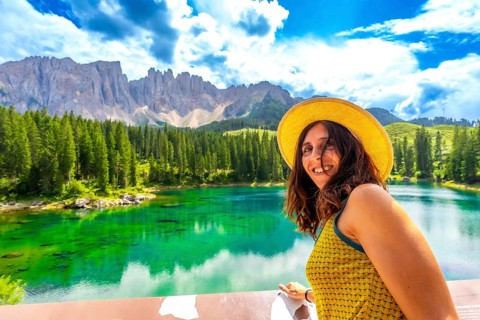 Tourist admiring the stunning emerald waters of lake carezza, with the latemar mountain range in