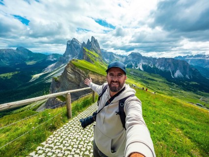 Photographer with backpack and camera taking a selfie with outstretched arm with the odle di eores