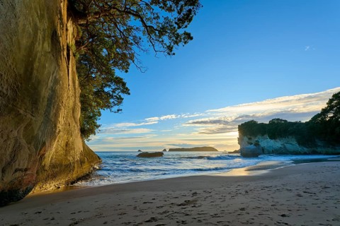 Beach with jagged rocks and calm sea, the sky is bathed in warm colours, Cathedral Cove,
