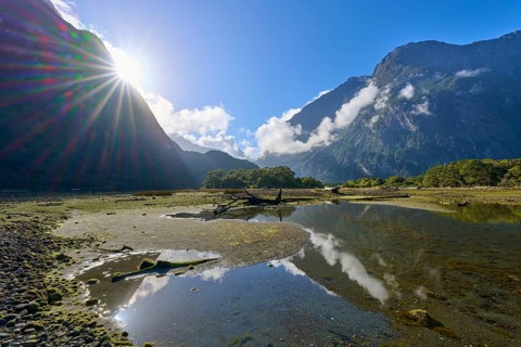 Dramatic sunbeams over mountains with clouds and water reflection, summer, Milford Sound, Te Anau,