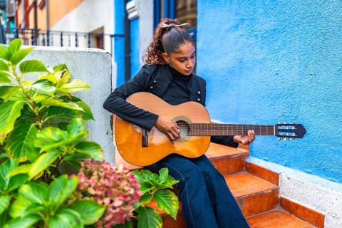 African american young beauty woman playing acoustic guitar outside a colorful house
