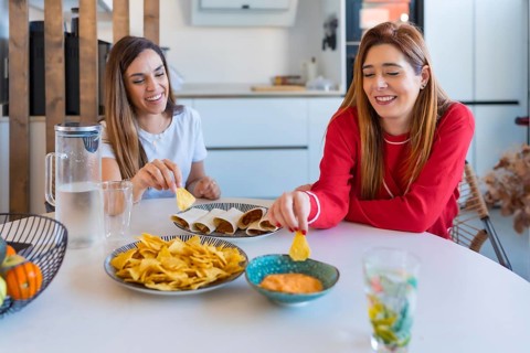 Two cheerful women enjoying a meal of quesadillas, nachos and sauce, creating a cozy and joyful
