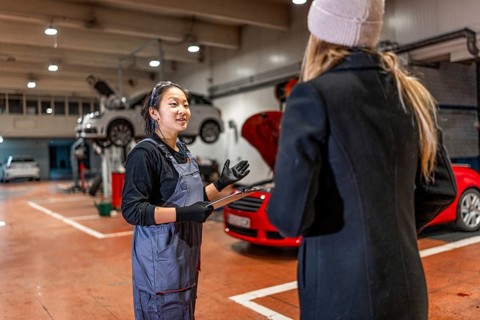 Professional female mechanic explaining car repair details to customer, holding clipboard in auto