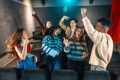 Cheerful multi ethnic friends dancing and enjoying music during movie disco event in cinema theater