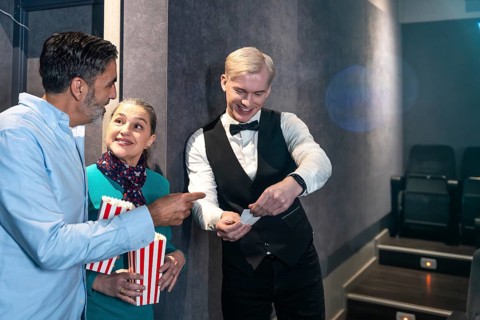Couple holding popcorn buckets showing their tickets to the usher before entering the movie theater