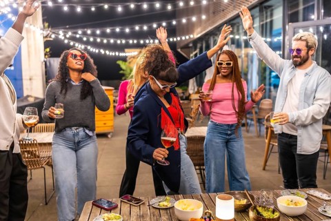 Caucasian woman drinking beer and dancing with multi-ethnic friends at outdoor night party