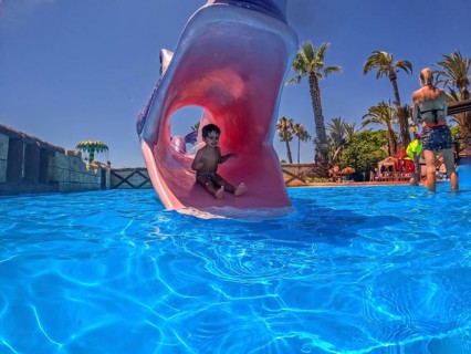 Young boy enjoying summer vacation sliding down a waterslide shaped like a monster's mouth into a