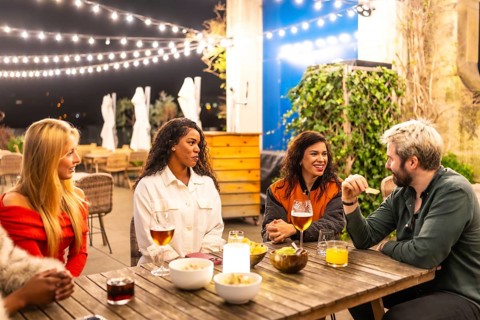 Multi-ethnic male and females friends talking relaxed drinking alcohol and eating snacks in a night