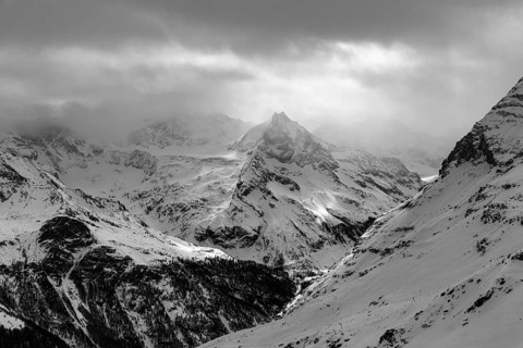 Dark clouds and wafts of mist surround the snow-covered summit of Mount Le Besso, view from the