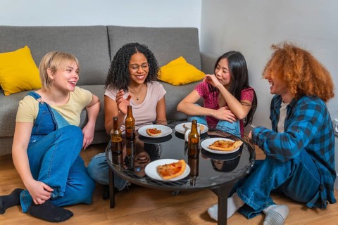Group of young multi ethnic friends laughing and eating pizza and drinking beer, sitting around a