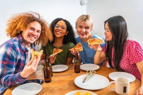 Four young, cheerful friends of diverse backgrounds enjoying pizza and beer together at home,