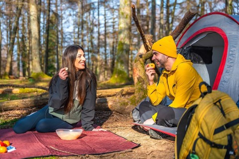 Hikers enjoying a healthy snack of fruit during a camping trip in a sunny forest, promoting a