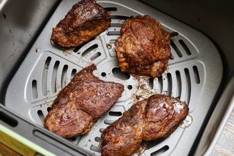 Juicy beef steaks rest inside an air fryer basket after cooking. The perfectly seared meat